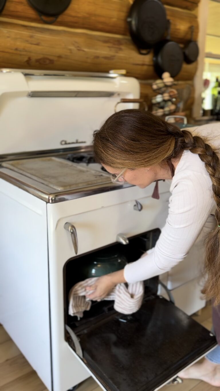 woman with long braided hair pulling roasting pan out of a white chambers stove